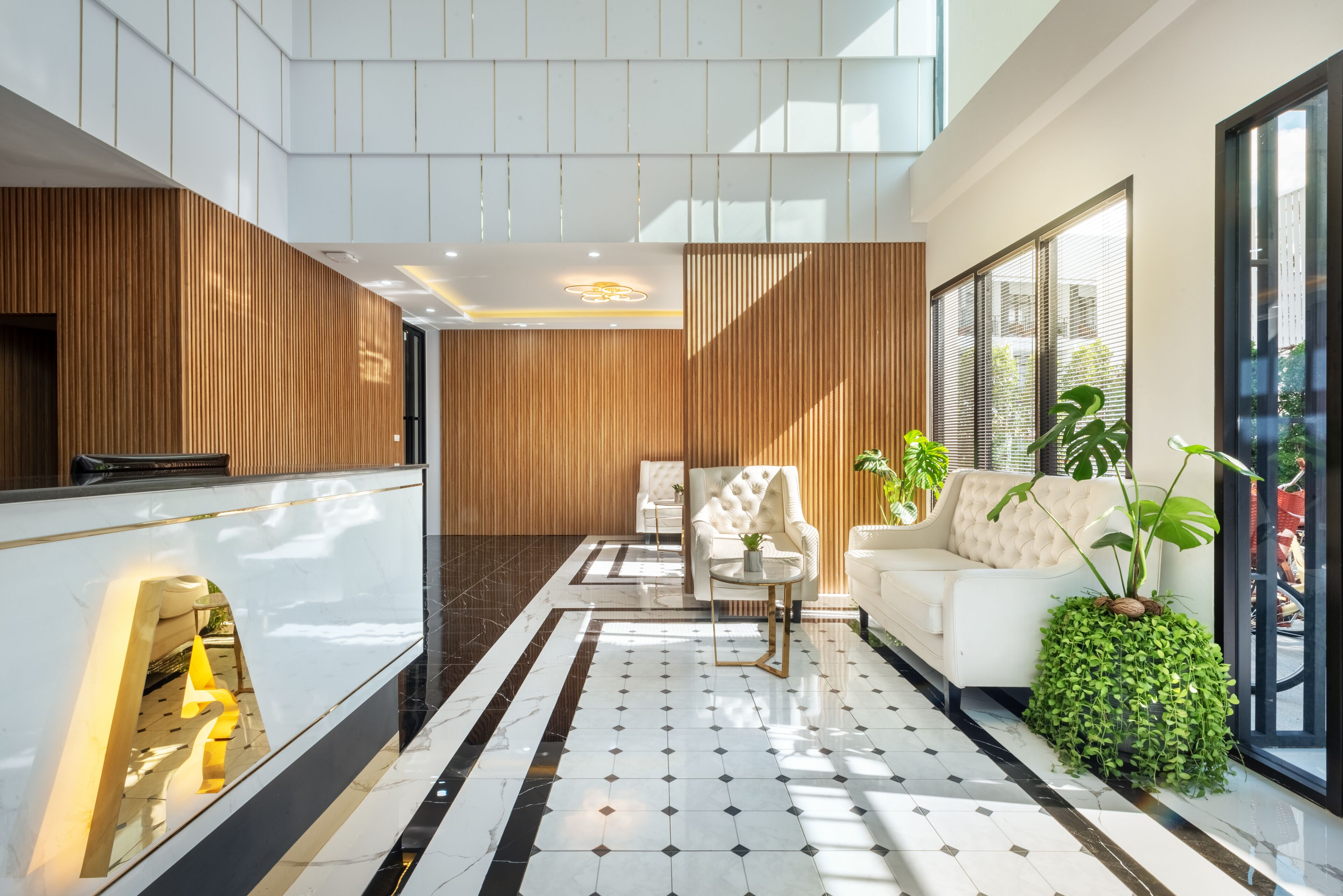 A modern lobby with a reception desk, a white sofa, a small table, and potted plants.