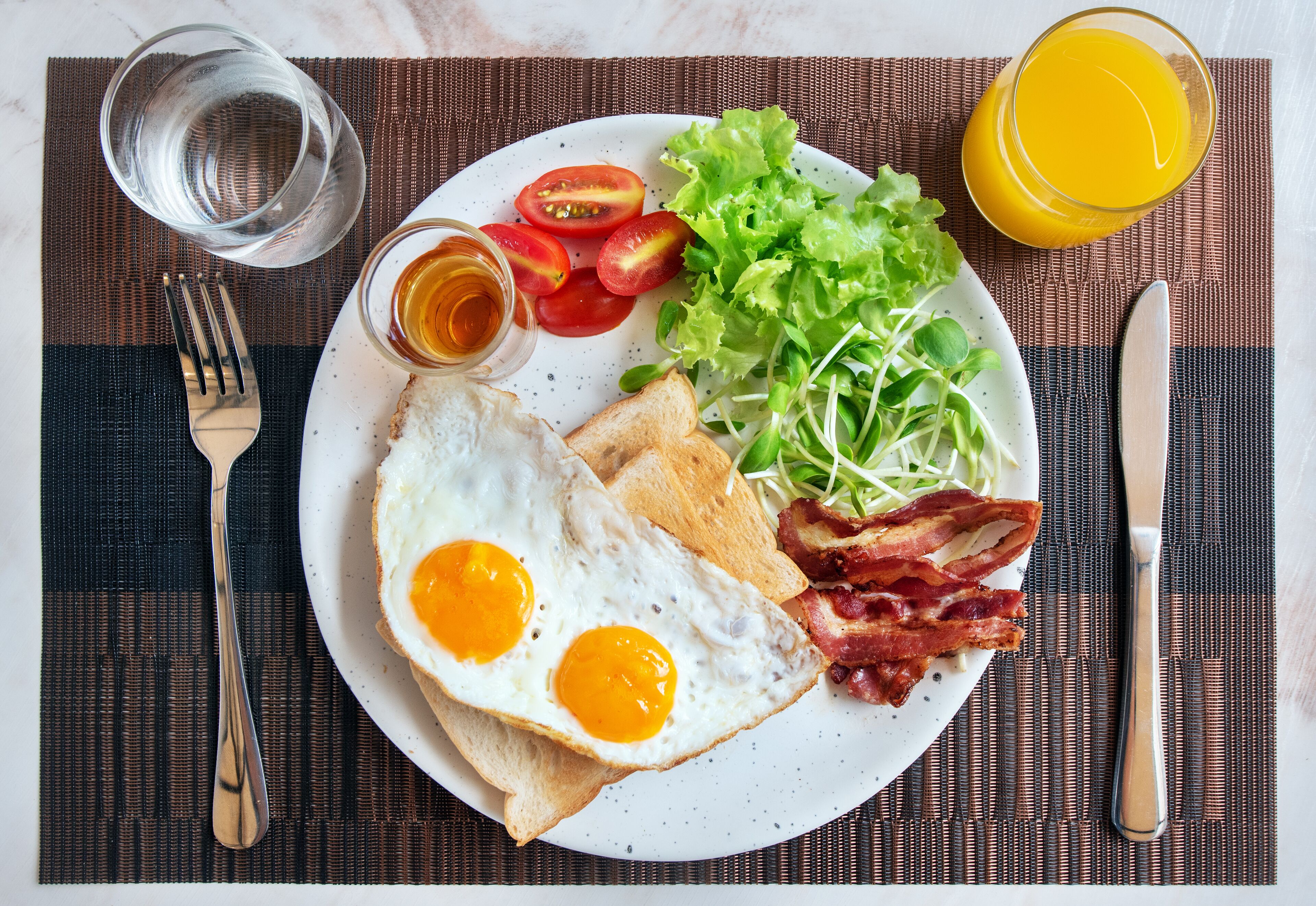 A breakfast plate with eggs, bacon, toast, tomatoes, lettuce, and a glass of orange juice.