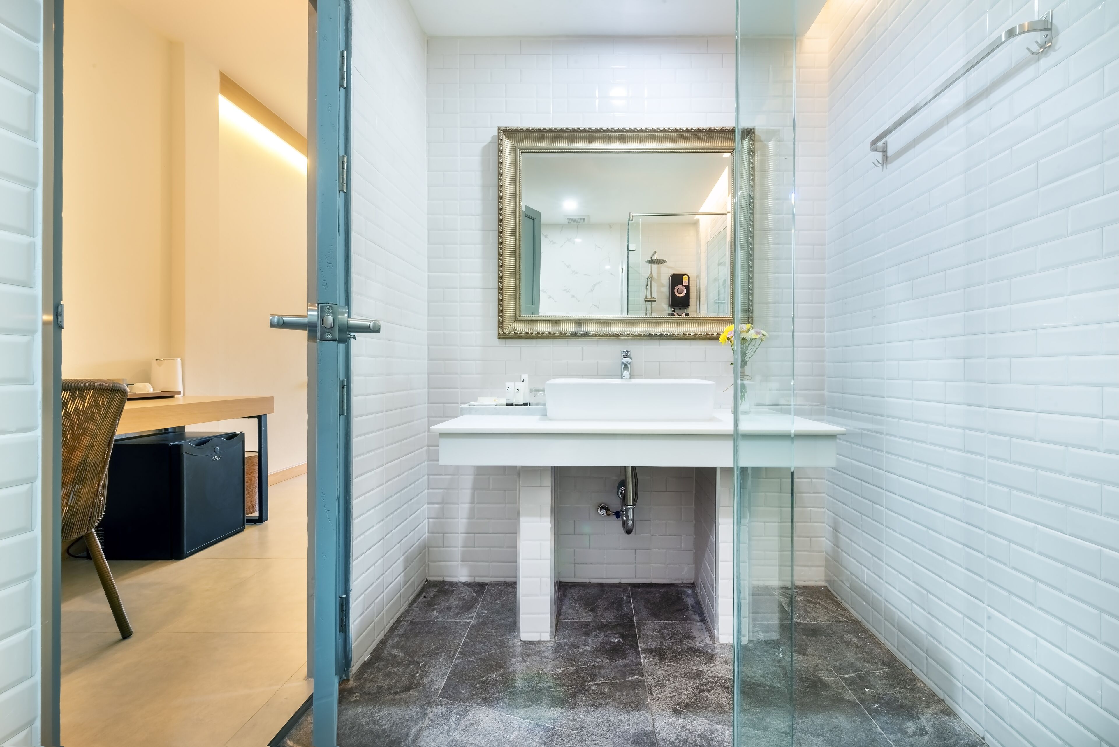 A modern bathroom with white tiled walls, a glass shower enclosure, and a white sink with a gold-framed mirror above it.