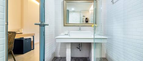 A modern bathroom with white tiled walls, a glass shower enclosure, and a white sink with a gold-framed mirror above it.