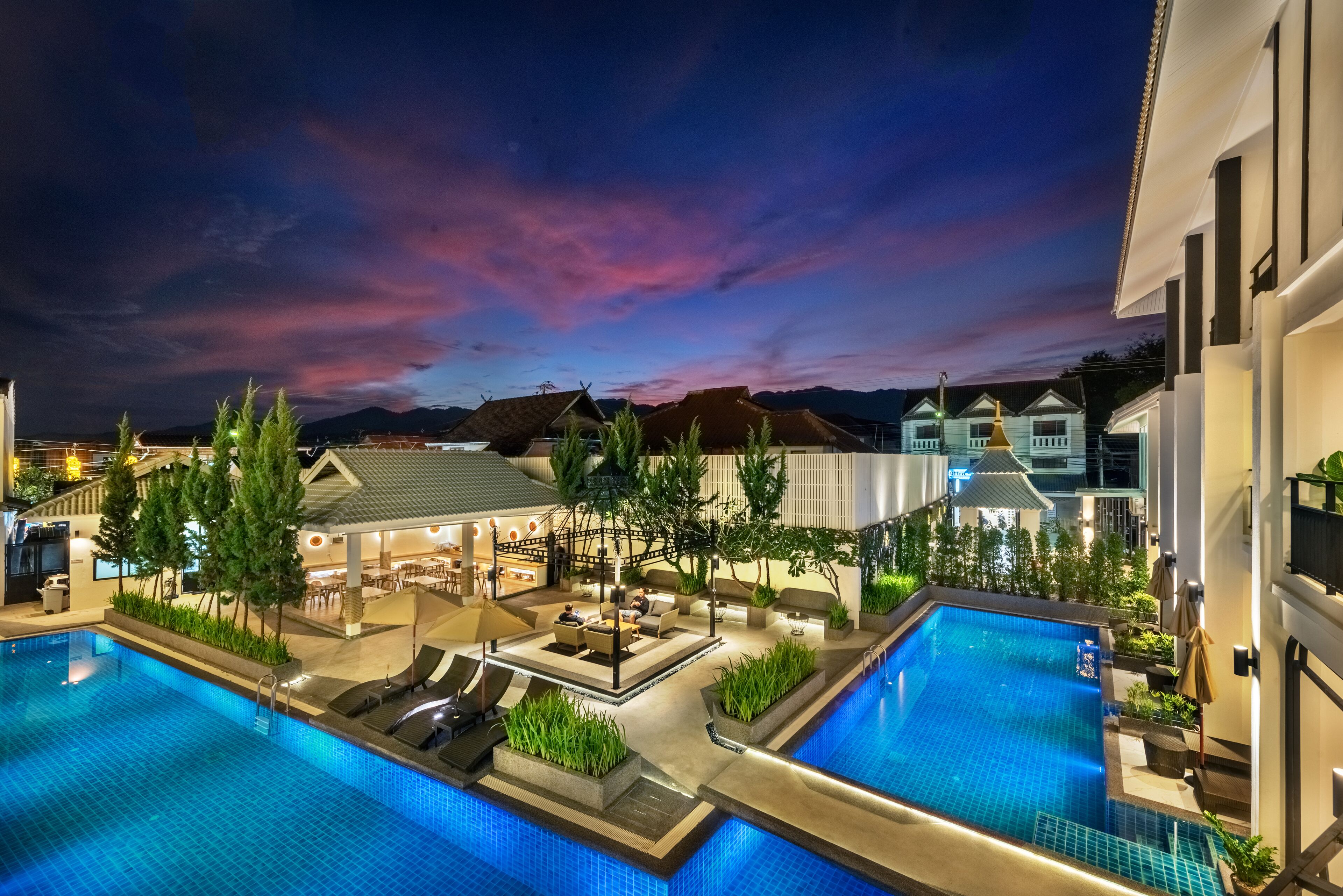 A rooftop pool area with lounge chairs and a bar, surrounded by buildings and a mountainous backdrop.