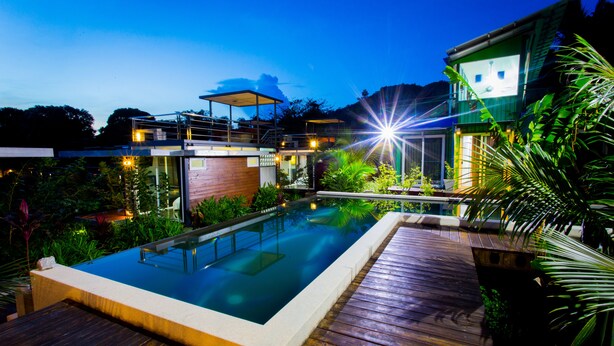 A swimming pool with a wooden deck, surrounded by lush greenery and modern architecture. - Baan Boom Boxes (Koh Samui)