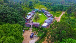 An aerial view of a resort with multiple buildings arranged in a semi-circle, surrounded by lush greenery. - Baan Boom Boxes (Koh Samui)