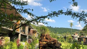 A modern house with a stone staircase, lush garden, and a view of the surrounding hills. - Baan Boom Boxes (Koh Samui)