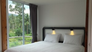A bedroom with a large bed, a view of palm trees, and a window with curtains. - Baan Boom Boxes (Koh Samui)