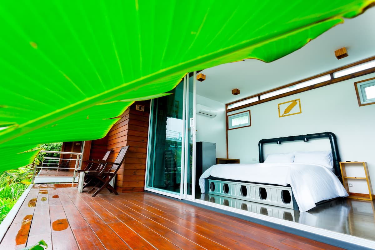 Una habitación con una cama, un ventanal corredero, una terraza de madera y un dosel verde.