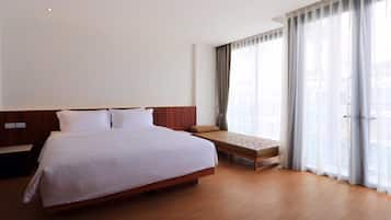 A modern hotel room with a large bed, a bench, and large windows with sheer curtains.