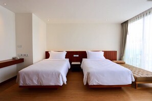 A hotel room with two single beds, a wooden headboard, a bedside table with a lamp, and a large window with curtains. - Varinah Resort (Sam Roi Yot)