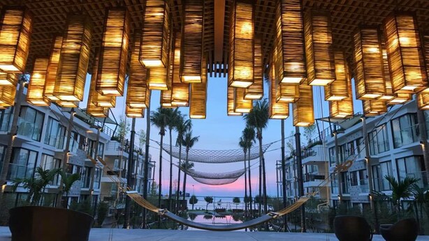 A modern hotel atrium with a hammock, palm trees, and a view of the sunset. - Varinah Resort (Sam Roi Yot)