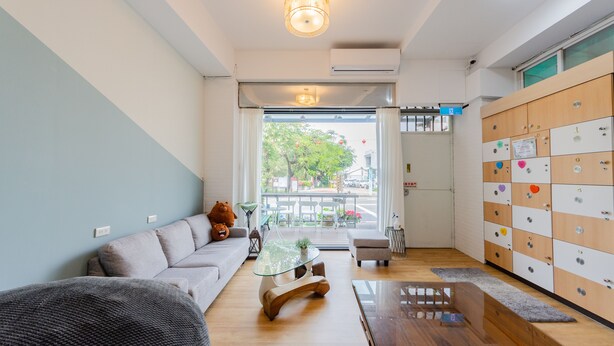 A modern living room with a sofa, a glass coffee table, and a wooden side table. There is a view of the outside through a glass door. - Tainan Anping Bailuwan House (Tainan)