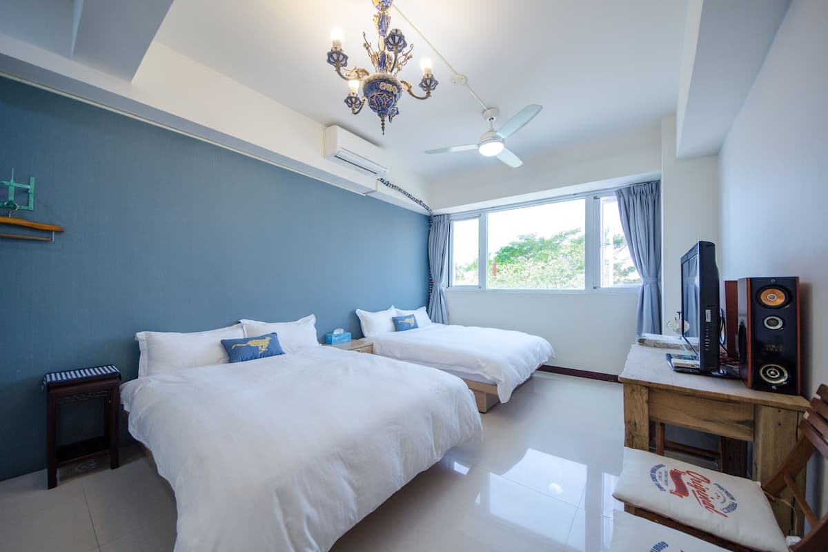 A hotel room with two beds, a ceiling fan, a chandelier, a TV, and a window with curtains.
