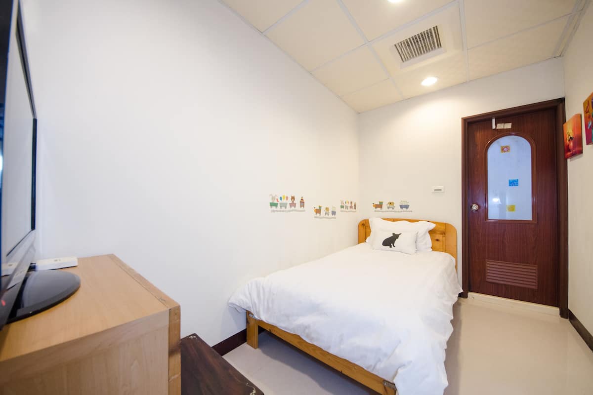 A bedroom with a wooden bed, white bedding, a desk with a computer, and a door with a mirror.