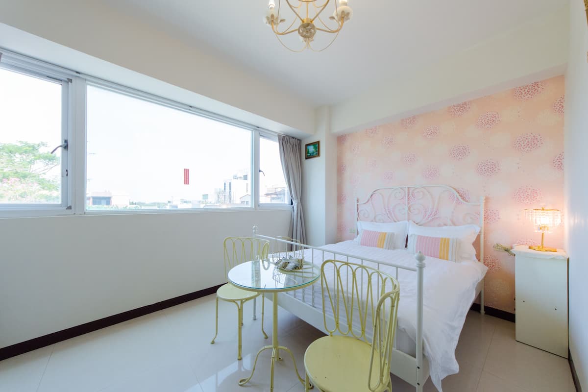 A hotel room with a bed, a small table, and chairs. There is a window with a view of buildings outside.