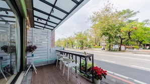 A wooden deck with tables and chairs, a glass enclosure, and a view of a street with trees and a scooter. - Tainan Anping Bailuwan House (Tainan)