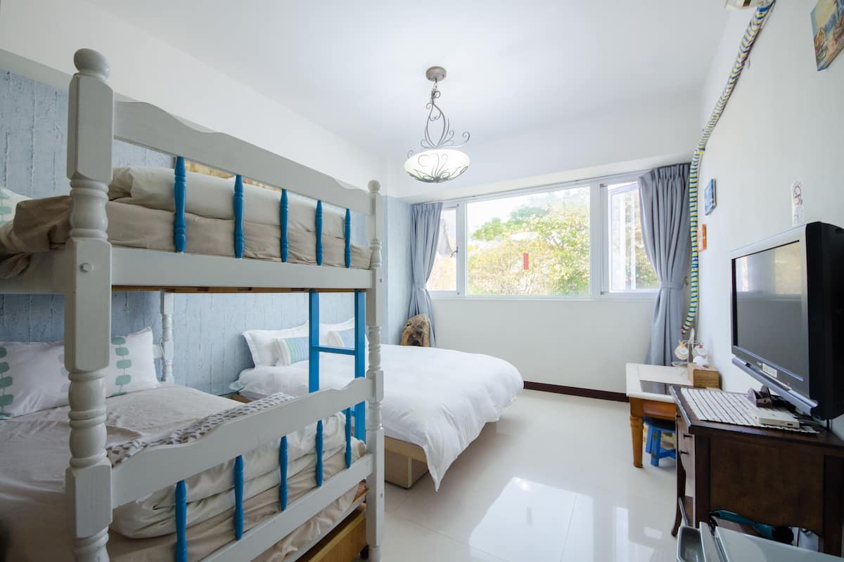 A bedroom with bunk beds, a desk with a computer, a TV, and a window with curtains.