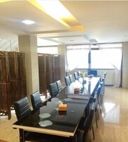 Un salón de conferencias con una larga mesa, sillas negras y un panel de vidrio.