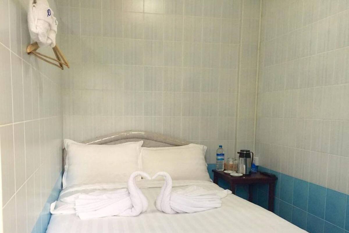 A hotel room with a bed, pillows, a bedside table with a water bottle, a coffee maker, and a towel rack with a towel.