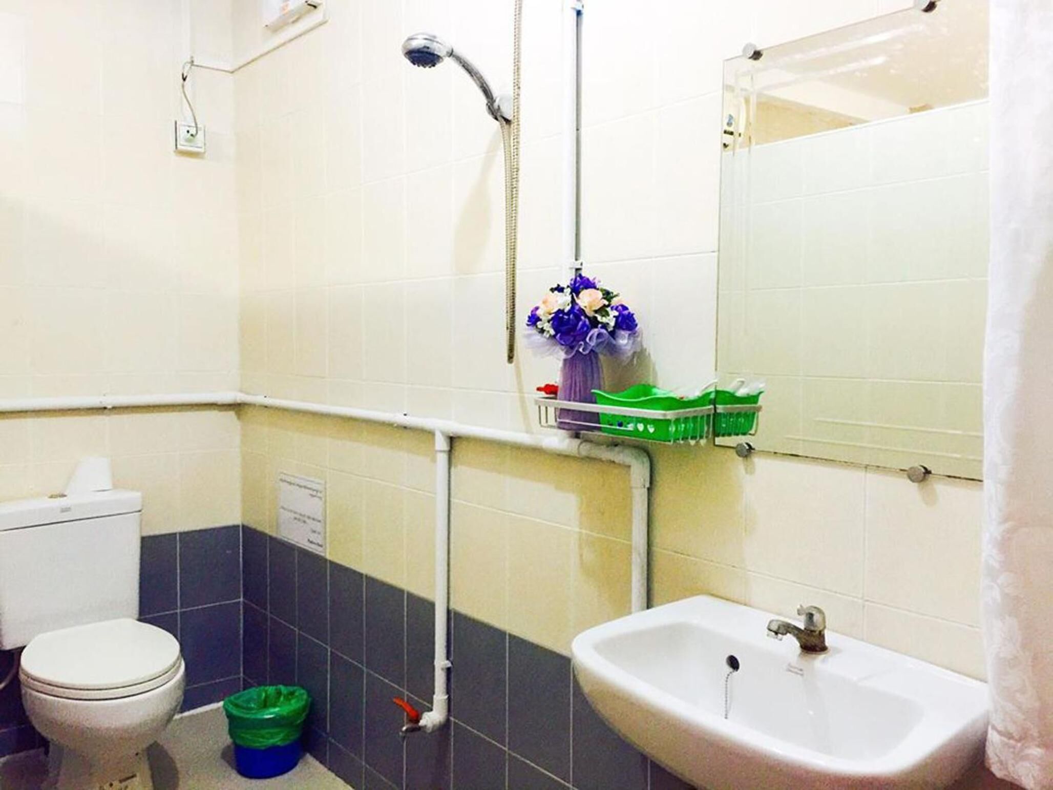 A bathroom with a toilet, sink, shower, and a green basket on the wall.