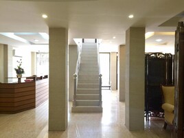 Un vestíbulo de hotel con una escalera central, una recepción y una zona de estar.