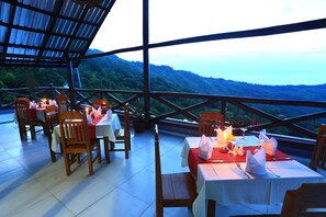 An outdoor dining area with tables set for two, surrounded by wooden chairs, overlooking a mountainous landscape. - The Floral Breeze Hotel Mt.Victoria (Kanpetlet)