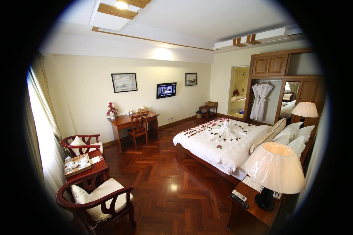 Une chambre d’hôtel avec un plancher en bois, un lit avec une literie blanche, un bureau avec une chaise, une télévision et un miroir.