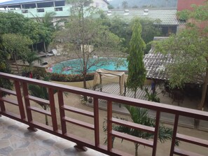 Vista de una piscina rodeada de vegetación, con suelo de baldosas y una valla de madera al frente.