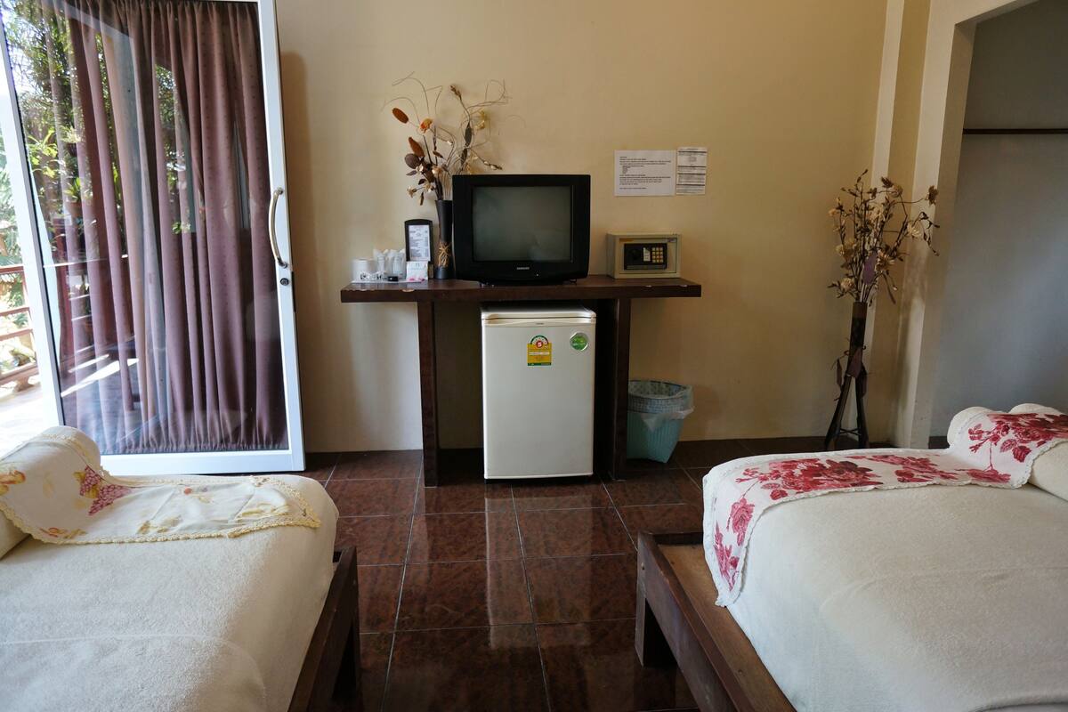A hotel room with two beds, a small refrigerator, a television, and a desk with a vase of flowers.