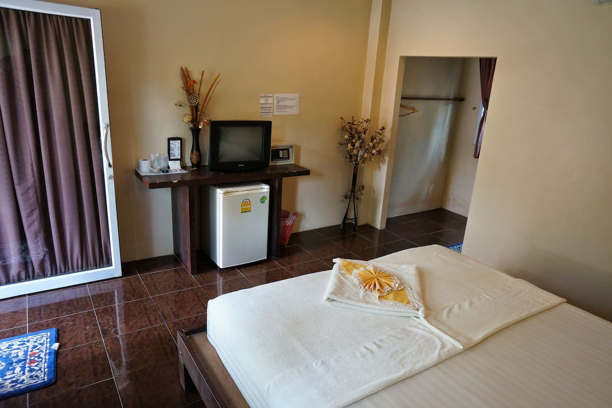 A hotel room with a bed, a desk with a television, a refrigerator, and a vase with dried plants.