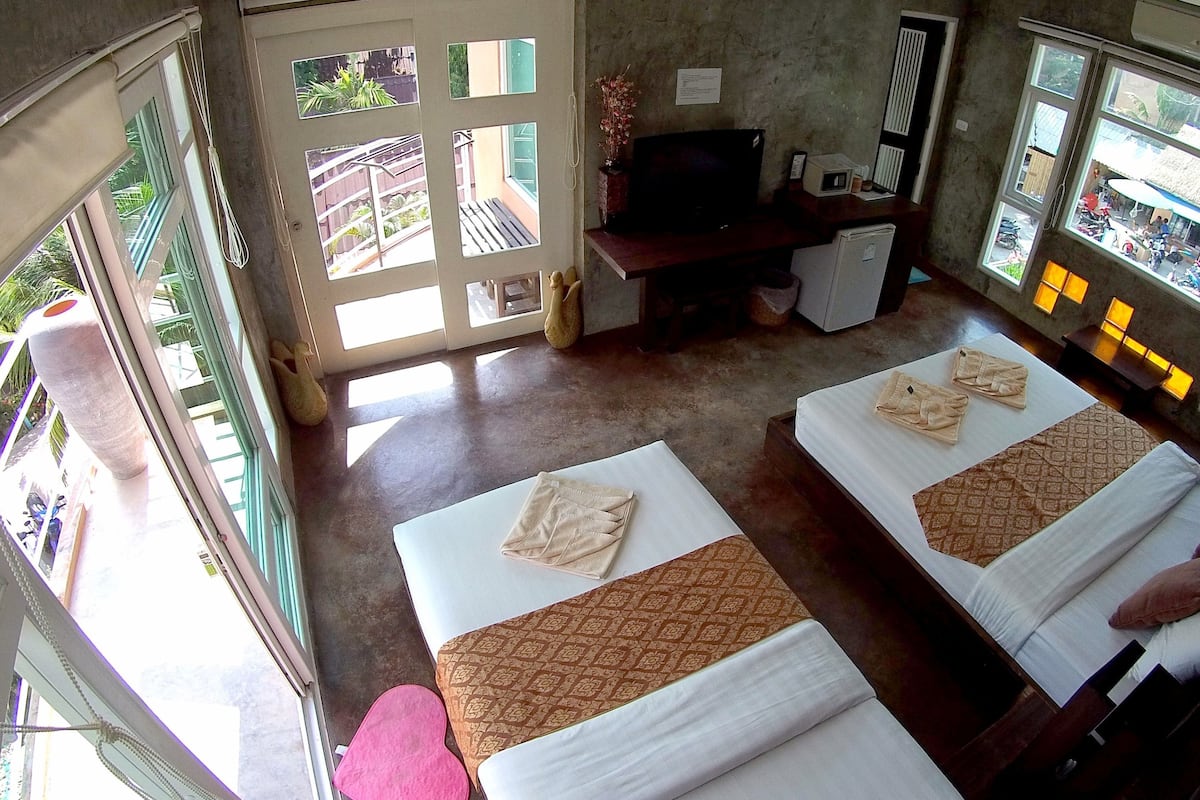 A hotel room with two beds, a desk with a television, and large windows offering a view of the outside.