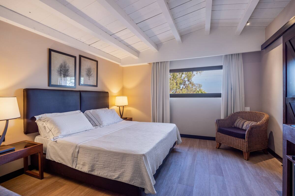 A hotel room with a large bed, a nightstand, a chair, and a window with curtains.