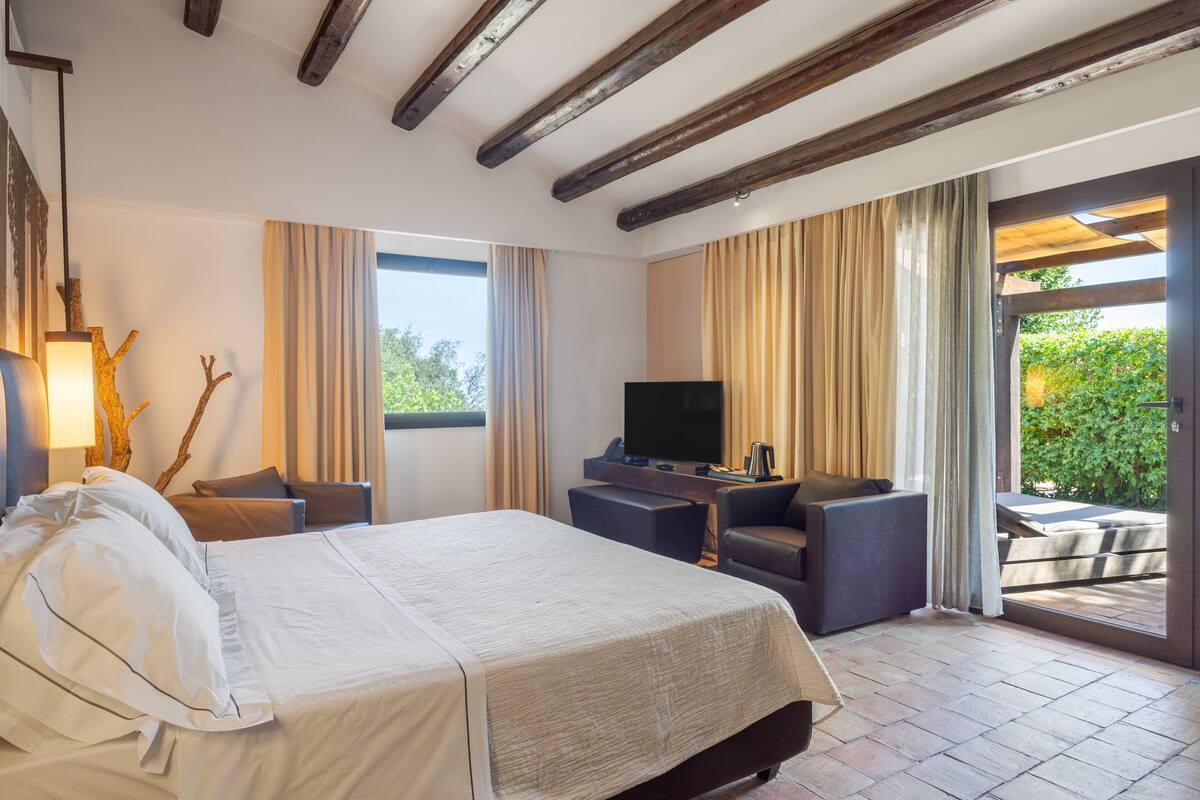 A hotel room with a bed, a TV, a sofa, and a balcony with curtains.
