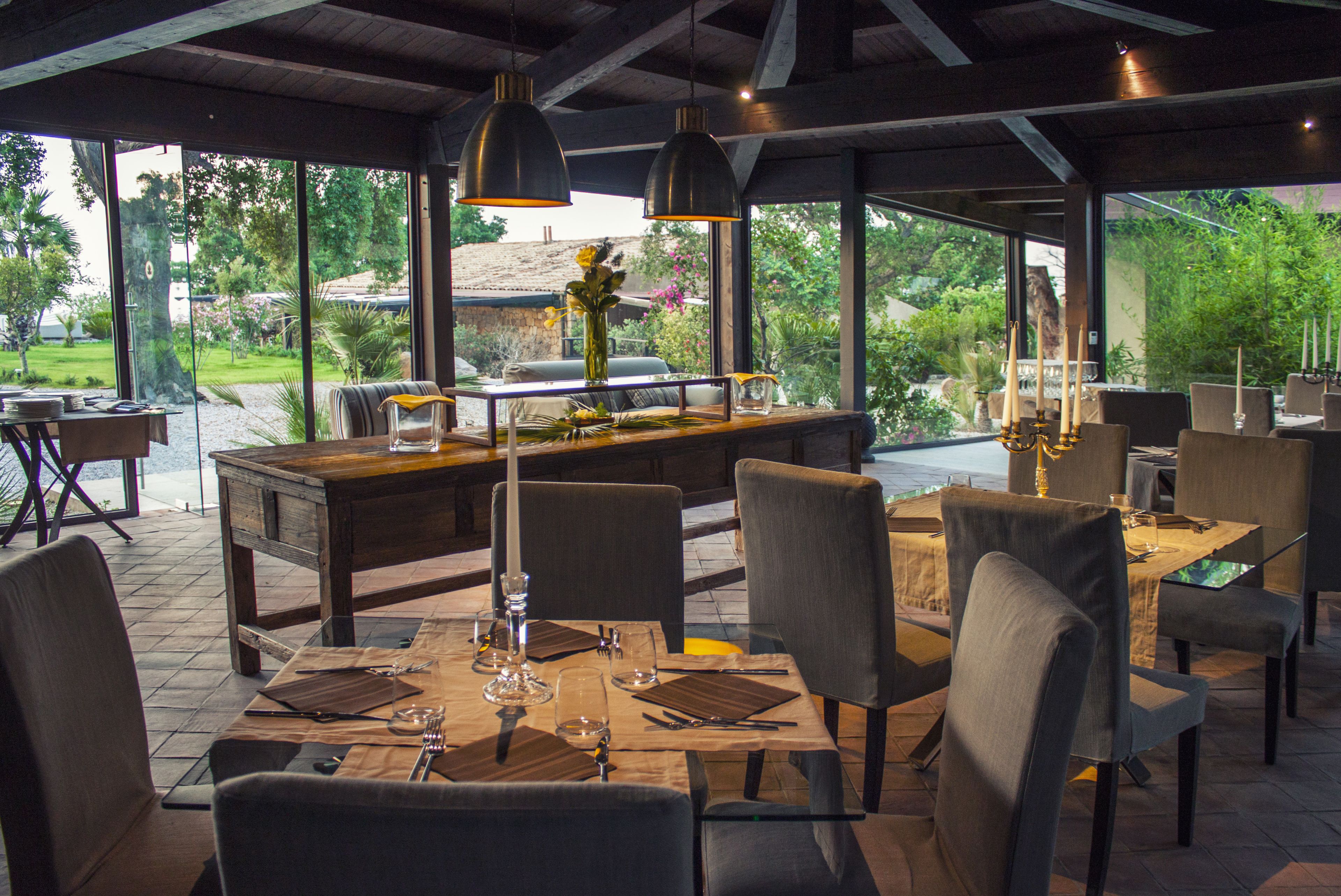 An outdoor dining area with a wooden table and chairs, large windows, and a view of the garden.