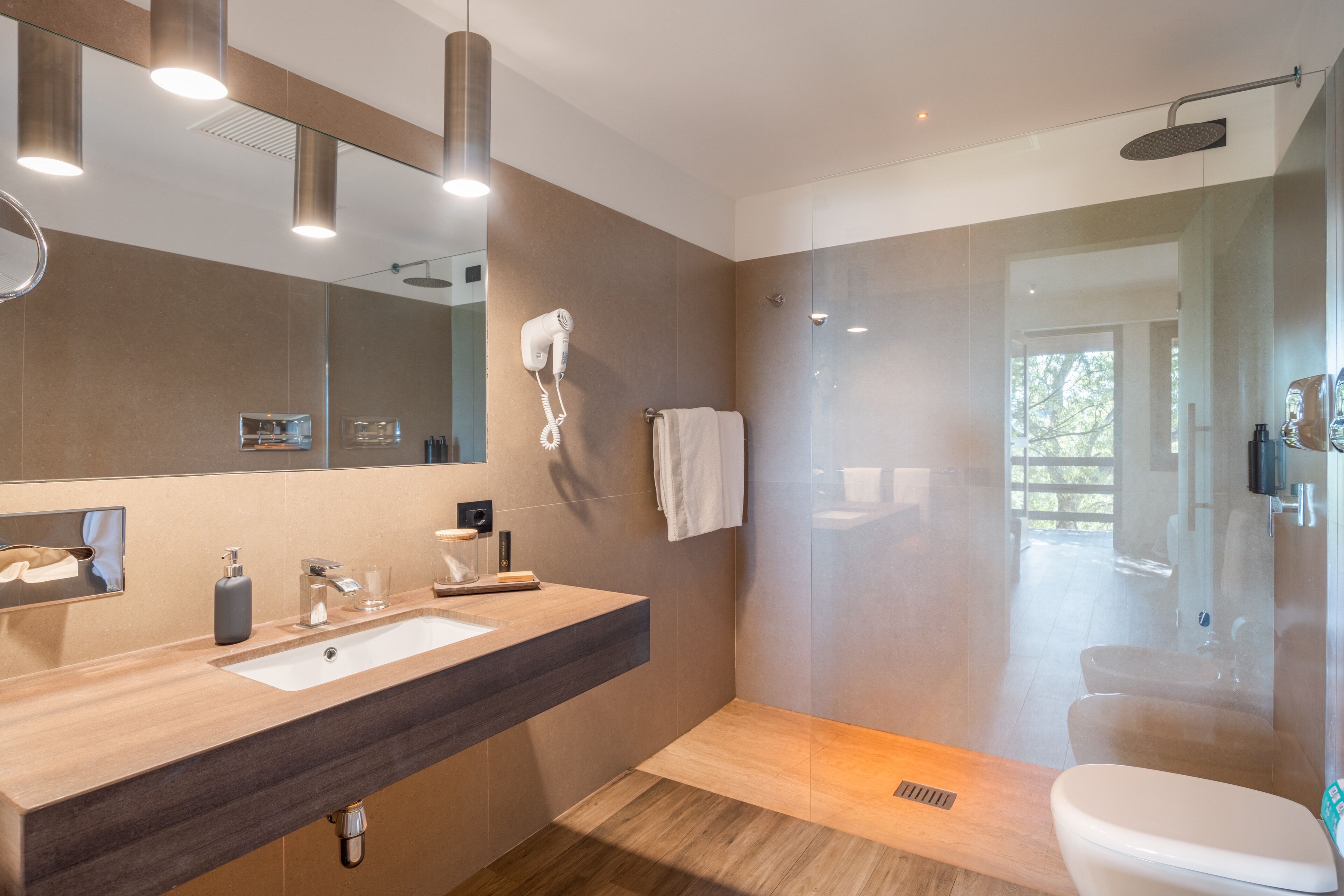 A modern bathroom with a large mirror, a vanity with a sink, a hairdryer, and a glass-enclosed shower area.