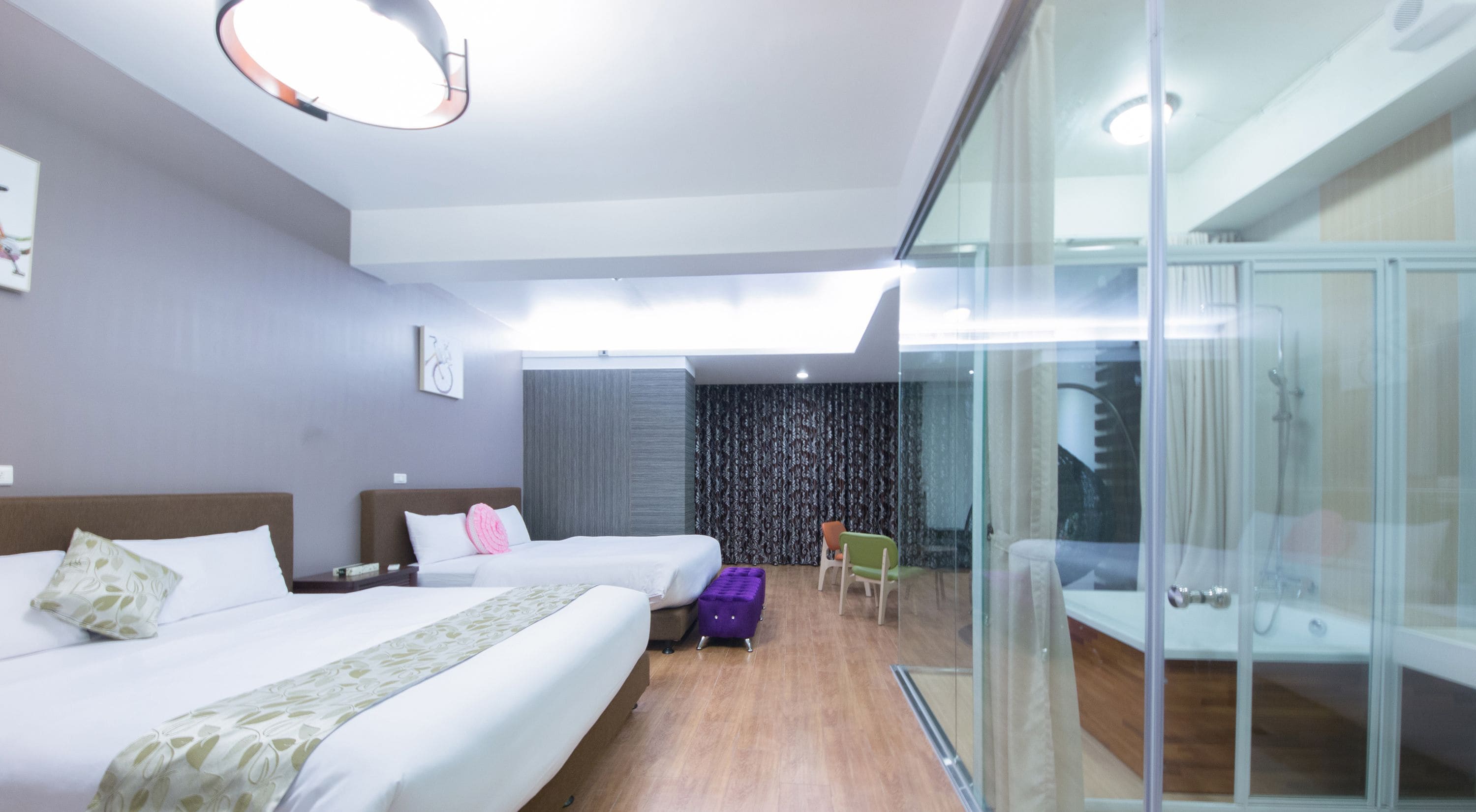 A hotel room with two beds, a small table, a chair, and a glass partition.