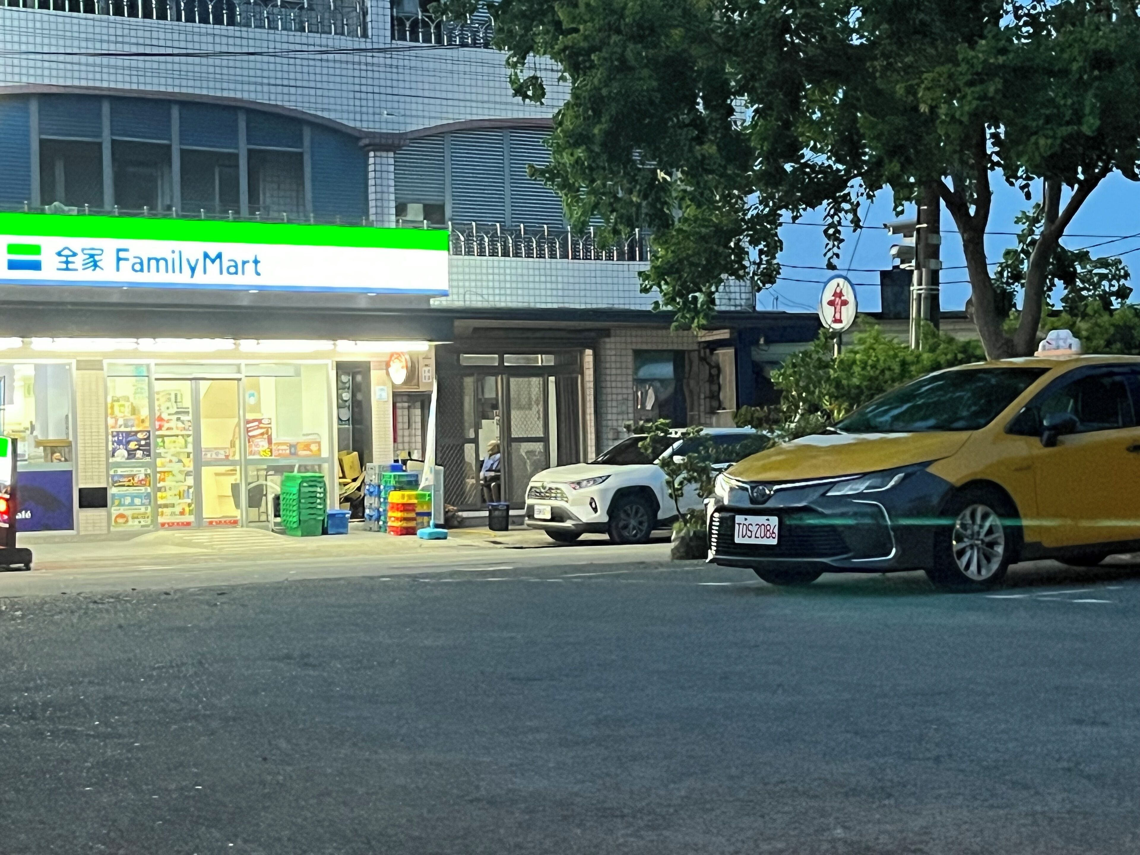 A FamilyMart store with a visible entrance, a parking area, and a yellow car parked in front.