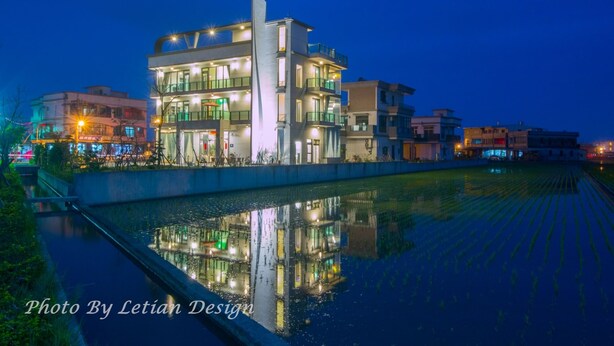 A modern building with multiple floors and balconies, reflecting in a water body. - Tsaiyu B&B (Zhuangwei)