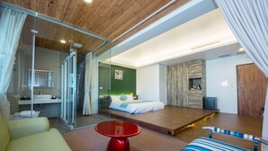 A modern hotel room with a glass shower enclosure, a bed with a wooden headboard, a red table, and a striped sofa. - Tsaiyu B&B (Zhuangwei)