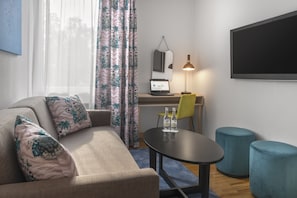A modern living room with a sofa, a desk with a laptop, a lamp, and two ottomans.