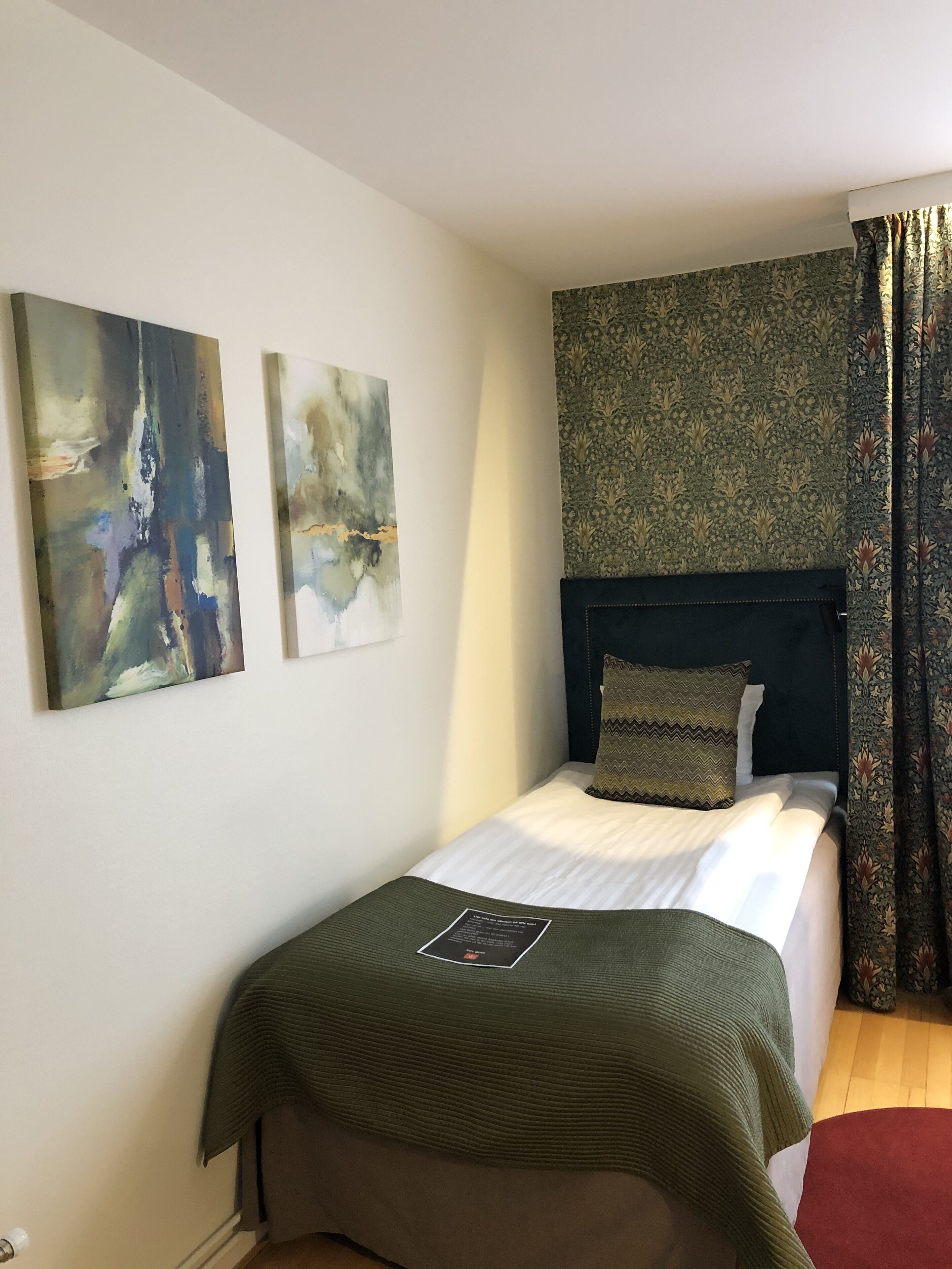 A bedroom with a bed, two abstract paintings, a patterned wall, and a dark headboard.