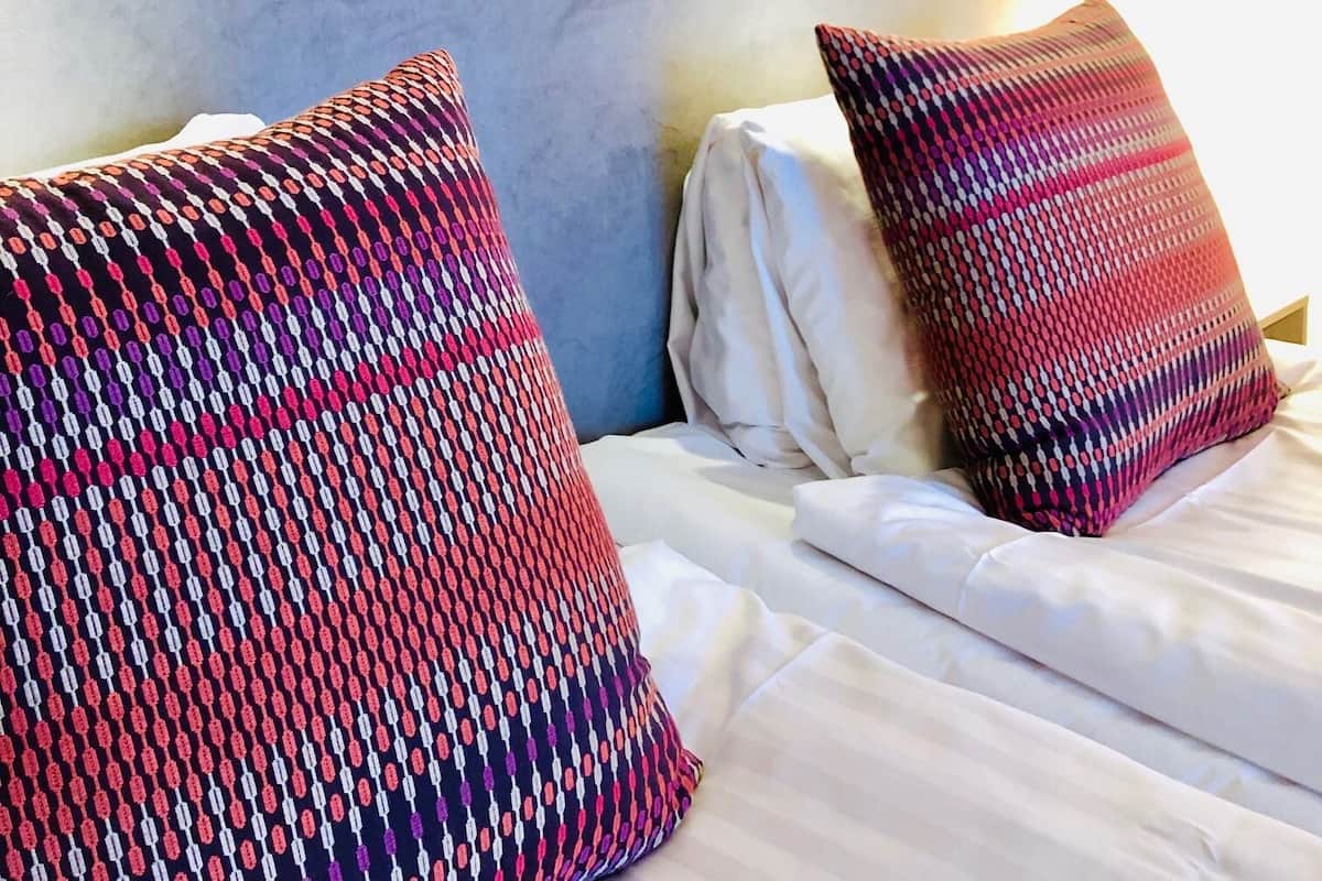Quarto de hotel com cama, duas almofadas estampadas e um mural floral na parede.