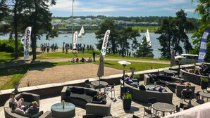 An outdoor seating area with wicker furniture, a view of a lake, and flags with the text "ADPRO". - Skogshem & Wijk (Lidingo)