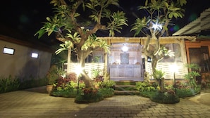 A well-lit outdoor area with a wooden structure, possibly a gazebo, surrounded by potted plants and a paved walkway. - Batu Empug Ubud Cottages (Ubud)