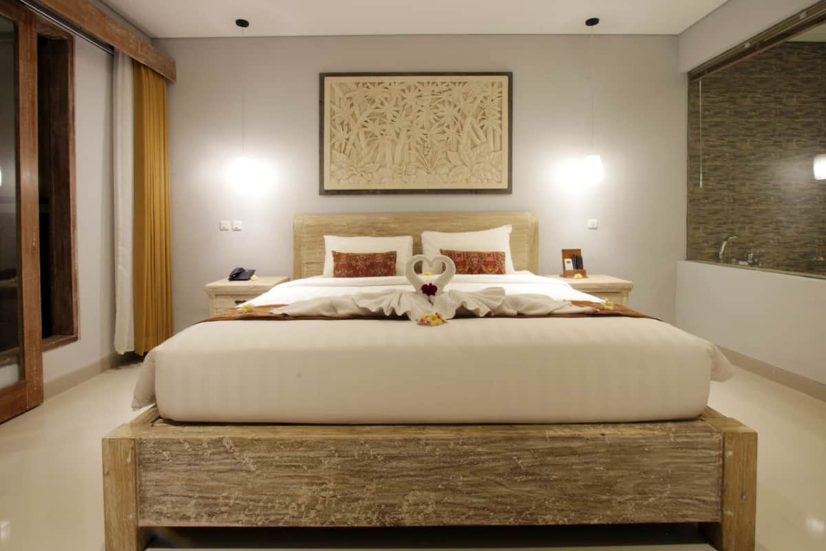 A neatly made bed with a wooden headboard, a wall-mounted artwork, and a large mirror.