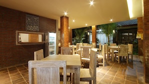 A restaurant with wooden tables and chairs, brick walls, and a tiled floor. - Batu Empug Ubud Cottages (Ubud)