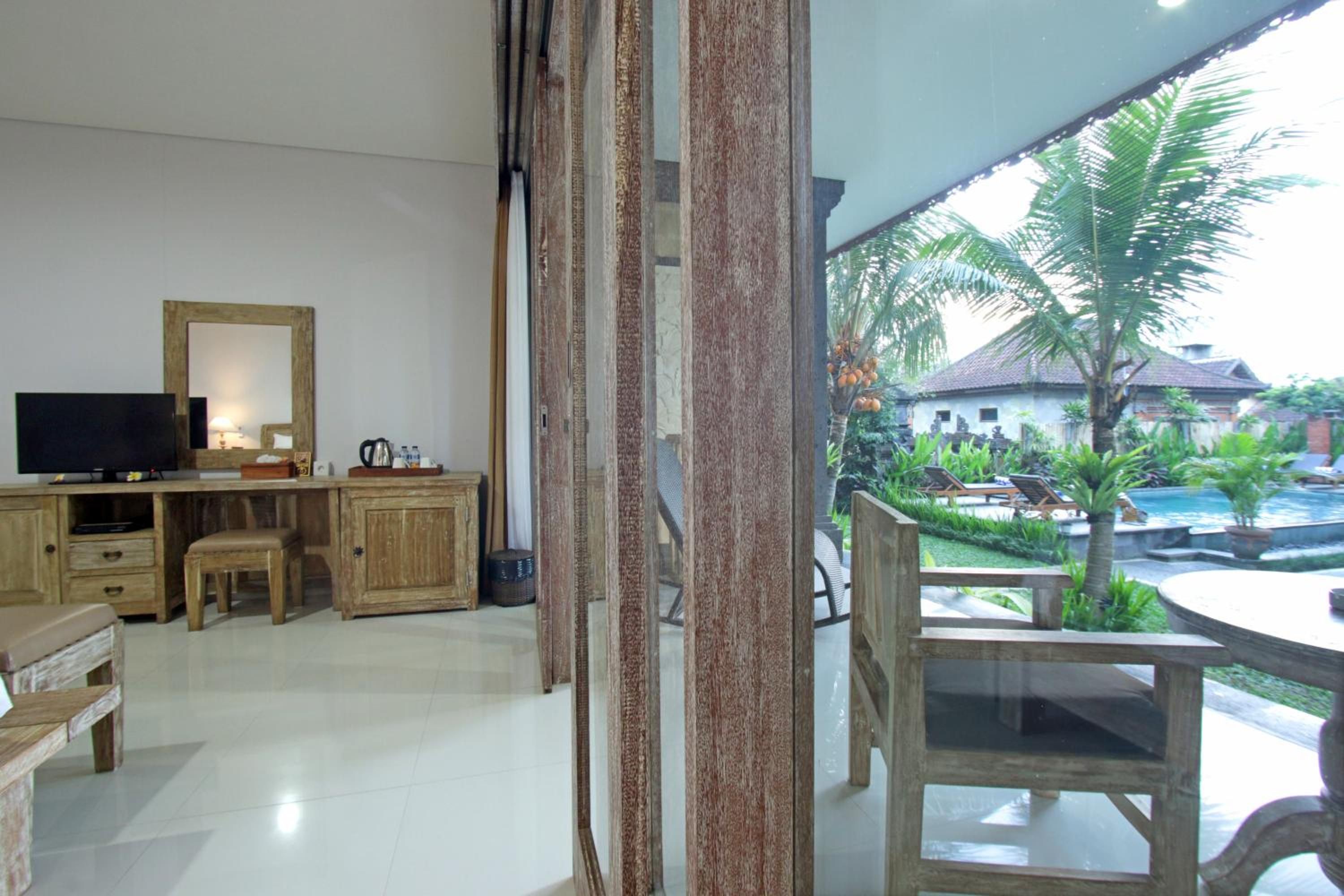 Ein Zimmer mit Fernseher, Holzmöbeln und Blick auf einen Innenhof mit Pool und Palmen.