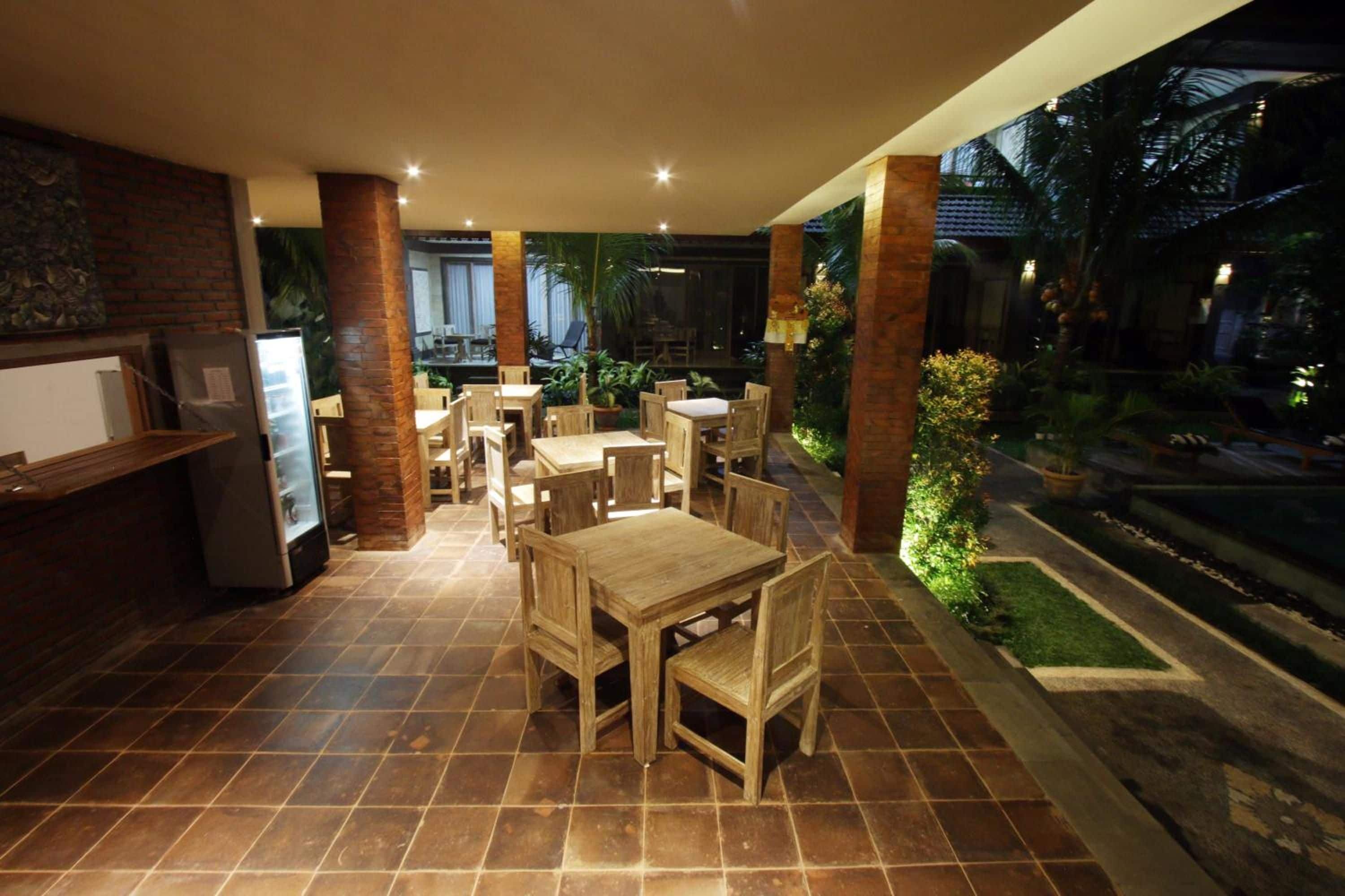 An outdoor dining area with wooden tables and chairs, surrounded by brick pillars and potted plants.