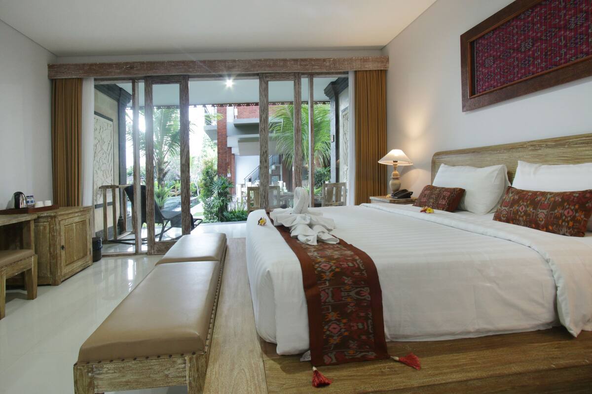 A hotel room with a large bed, a bench, a desk, and a view of the outdoors.
