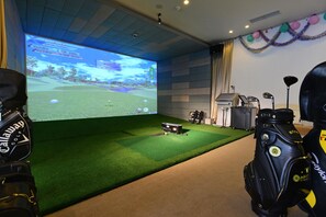 Ein Raum mit einem großen Bildschirm, der ein Golf-Simulationsspiel zeigt, einem Grünbereich und Golfbags.