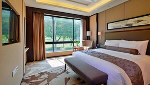 A hotel room with a large bed, a bench, a desk, and a view of greenery outside. - Kylin villa (Shenzhen)