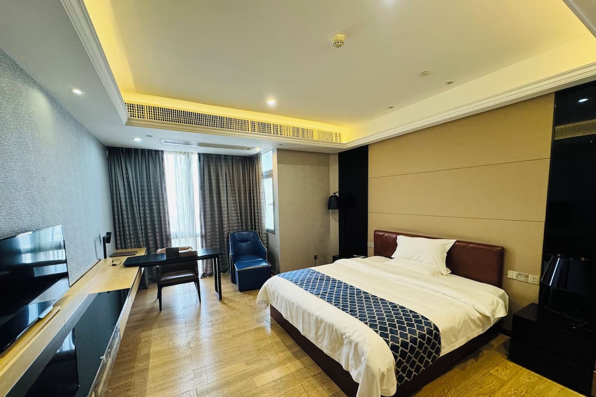 A hotel room with a bed, a desk, a chair, a TV, and a window with curtains.